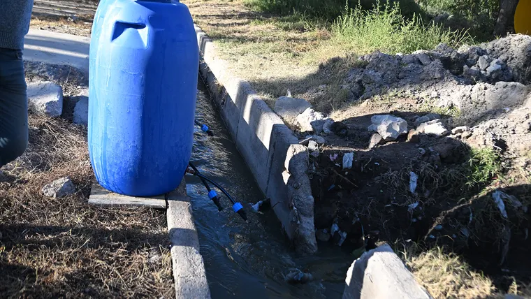 Acequia rota con efluentes cloacales y bidón azul de agua junto a una vivienda en Los Corralitos, Mendoza