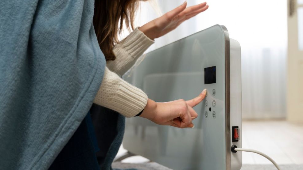 Mujer calefaccionando con convector eléctrico en invierno