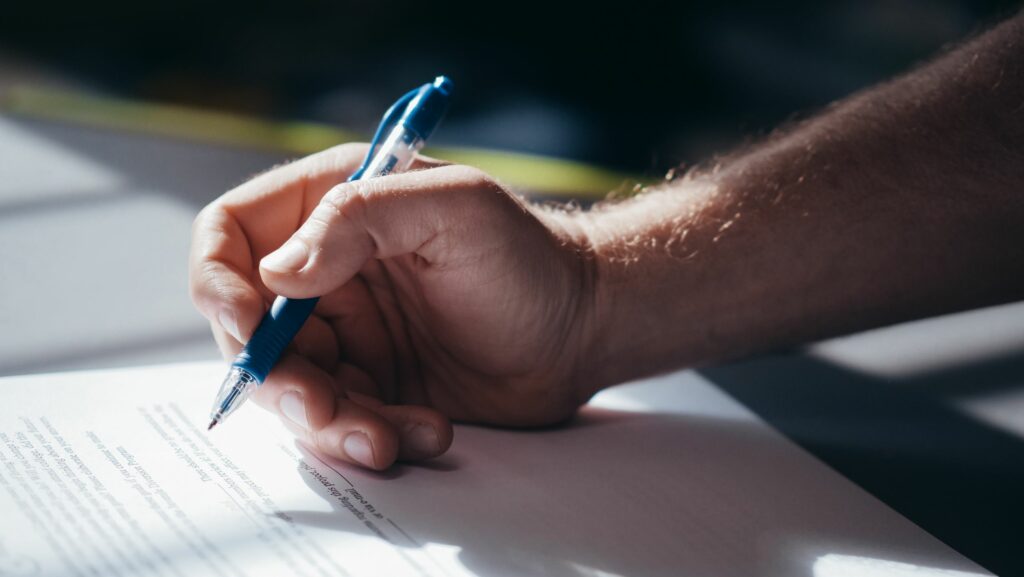 Persona firmando contrato de plan de ahorro vehicular en una concesionaria con documentos sobre la mesa