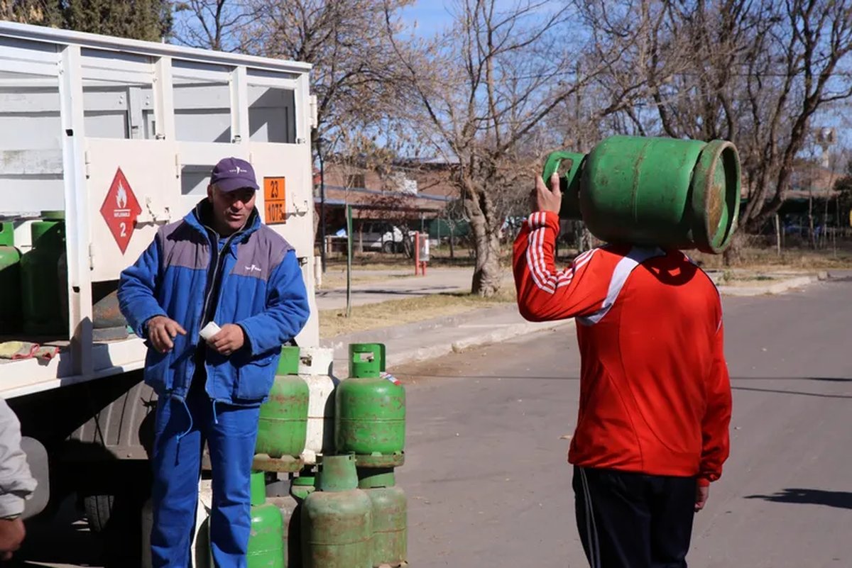 Reparto de garrafas de gas de 10 kilos en la calle; un vecino carga una garrafa al hombro